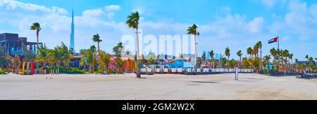 Panorama von La Mer weißen Sandstrand mit einer Reihe von Palmen, Strandläden, Cafés und die Silhouette des Burj Khalifa im Hintergrund, Dubai, VAE Stockfoto