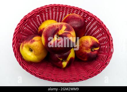 Reife Pfirsiche in einem roten Korb isoliert auf weißem Hintergrund Stockfoto