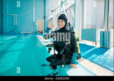 Weibliche Taucherin im Tauchanzug, die am Pool sitzt Stockfoto