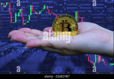 Frau Hand hält goldene Bitcoin Kryptowährung an Computer-Trading-Chart Hintergrund, Digital Money Konzept Stockfoto
