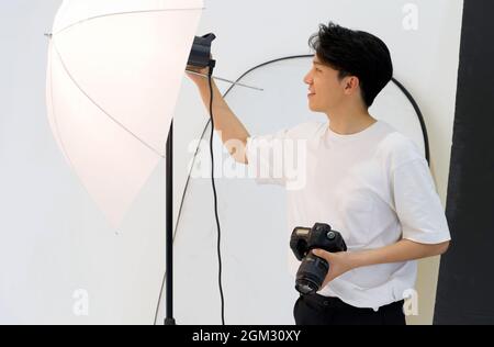 Asiatische Fotografen passen die Helligkeit von Lichtern für die Aufnahme von Modemodellen im Studio an. Stockfoto