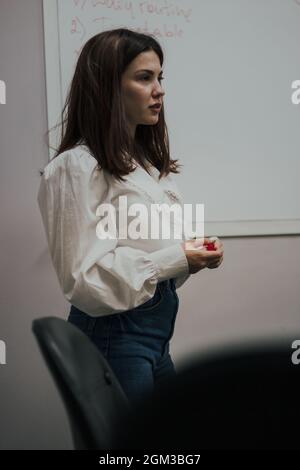 Junge Englischlehrerin mit einem roten Marker in einer weißen Bluse, die vor einem weißen Brett steht. Stockfoto