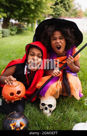 Gruselige afroamerikanische Kinder in halloween-Kostümen, die beim Spielen auf dem Hinterhof schreiend herumspielen Stockfoto