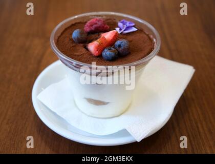 Hausgemachtes Tiramisu-Dessert garniert mit Erdbeeren und Blaubeeren mit Blumen Stockfoto