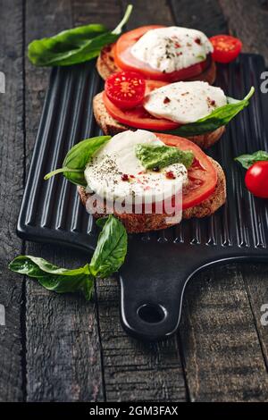 Offene Sandwiches oder Bruschetta mit Mozzarella-Käse, Tomaten und Basilikum, Caprese auf dunklem Holzhintergrund. Stockfoto