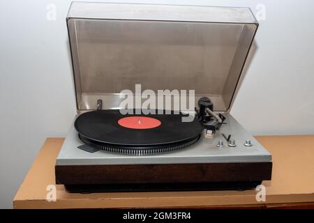 Analoger Vintage-Stereo-Plattenspieler im Retro-Stil auf einem Holztisch. Ein altmodischer Plattenspieler aus Kunststoff, der einen Musiktitel spielt, Vorderansicht. Retro-Musikkonzept Stockfoto