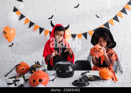 afroamerikanische Kinder in halloween Kostümen bereiten Trank im Hexenkessel vor Stockfoto