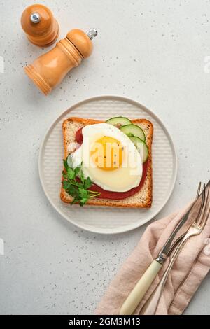 Toast mit Tomaten Ketchup, Gurke und Spiegelei auf weißem Teller, Draufsicht, grauer Hintergrund, Stockfoto