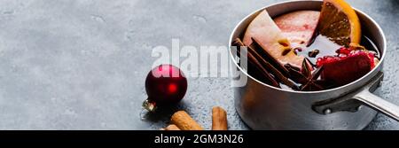 Glühwein-Heißgetränk mit Zitrus, Apfel, Granatapfel und Gewürzen in Aluminiumauflauf mit Vintage-Weihnachtsbaumspielzeug und Tannenzweig auf Betonbac Stockfoto