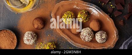 Vielfalt an hausgemachten dunklen Schokoladentrüffeln mit Kakaopulver, Pistazien, Mandeln in dunkelbrauner Hintergrundstruktur. Draufsicht, Kopierbereich. Stockfoto