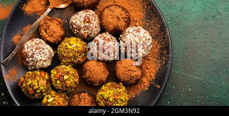 Vielfalt an hausgemachten dunklen Schokoladentrüffeln mit Kakaopulver, Pistazien, Mandeln in dunkelbrauner Hintergrundstruktur. Draufsicht, Kopierbereich. Stockfoto