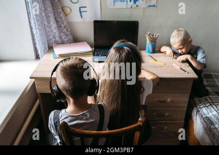Eine Gruppe von Schulkindern oder Freunden, die Kopfhörer tragen, sitzt zu Hause in der Nähe eines Laptops. Familie, Schüler Fernunterricht, virtuelle Online-Klasse auf Laptop Stockfoto