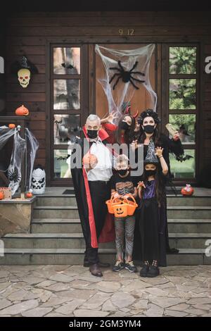 Gruselige Familie in halloween Kostümen und schwarzen medizinischen Masken, die schaurige Gesten in der Nähe der Veranda mit Dekoration zeigen Stockfoto