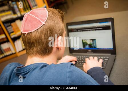 Jüdischer Junge, der Yarmulke von hinten trägt und in einem Klassenzimmer mit Schülern sitzt. Stockfoto