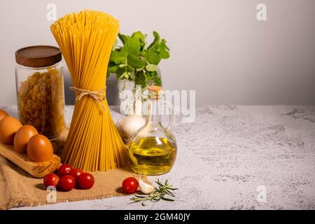Carbo-Diät - Spaghetti, Ditalini rohe Pasta zusammen mit einem Glas Olivenöl, cherri Tomaten, Knoblauch und Eier in Öko-Holz-Palette. Stockfoto