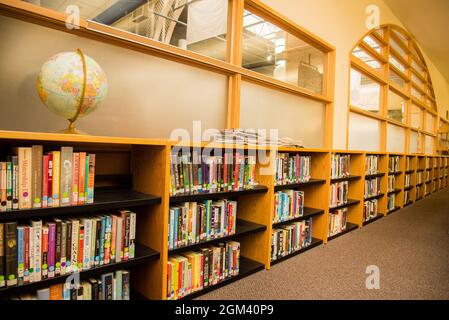 Regale mit bunten Büchern in einer Schulbibliothek mit einem Globus auf dem obersten Regal. Lerneinstellungen Stockfoto