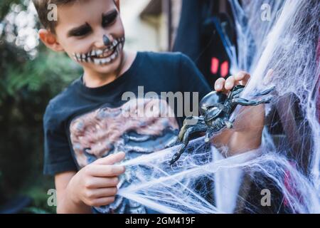 Verschwommener Junge im halloween Skelett Kostüm spielt mit Spielzeugspinne in der Nähe des dekorativen Spinnennetzes Stockfoto