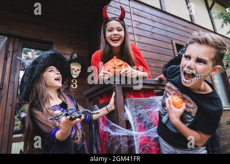 Fröhliche Kinder in gruseligen halloween Kostümen lachen auf der Haustreppe mit Dekoration Stockfoto