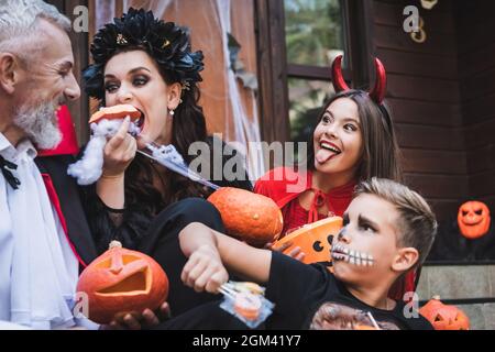 Frau, die rohen Kürbis in gruseligen halloween-Kostümen in der Nähe aufgeregter Familie isst Stockfoto