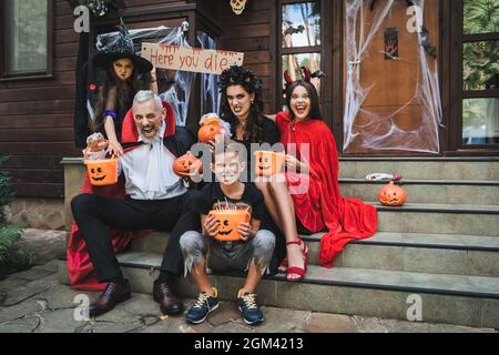 Eltern und Kinder in gruseligen halloween Kostümen knarren beim Sitzen auf der Hüttentreppe Stockfoto