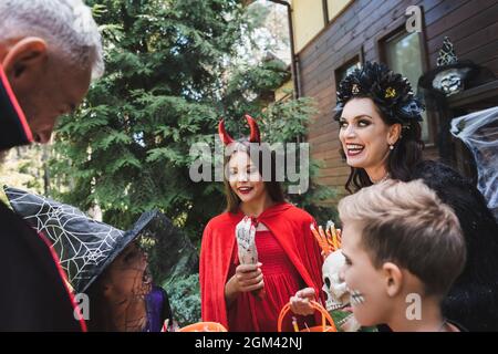 Fröhliches Mädchen hält Spielzeug Hand in der Nähe der Familie in gruseligen halloween-Kostüme Stockfoto