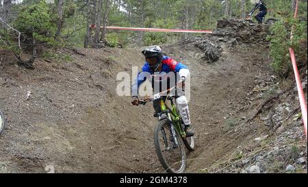 Ein Downhillfahrer, der während eines Rennens in Schutzausrüstung auf einer Strecke absteigt Stockfoto