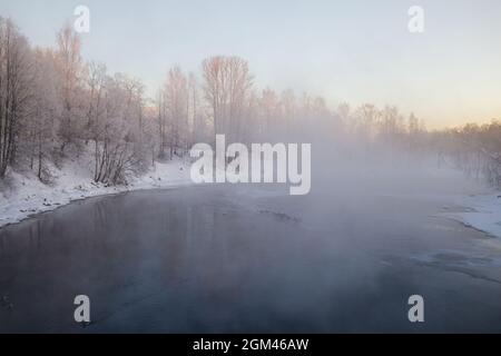 Natürlicher frostiger Winterhintergrund. Bei starkem Frost steigt Dampf über dem Wasser eines nicht-eisigen Flusses auf. Frühe Wintermorgendlandschaft Stockfoto