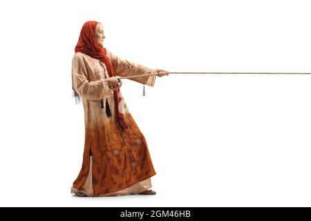 Ganzkörperaufnahme einer Frau in ethnischer Kleidung und einem Hijab, der ein auf weißem Hintergrund isoliertes Seil zieht Stockfoto
