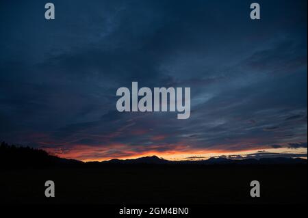 Wunderschöner, wolkiger Himmel, der in roten und orangen Farben des Sonnenuntergangs über der silhouettierten Natur gefärbt ist. Stockfoto