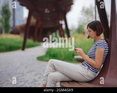 Schöne junge asiatische Frau, die am Sommertag Zeit im modernen Stadtpark verbringt. Stockfoto