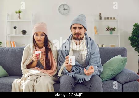 Das kranke junge Paar sitzt vor der Webcam in Decken gewickelt und mit einer Tasse Tee. Stockfoto