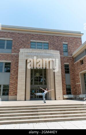 Selbstbewusste Schülerin auf dem College-Campus balancierte auf einem Bein, während sie sich vor dem Backsteingebäude zurücklehnte. Stockfoto