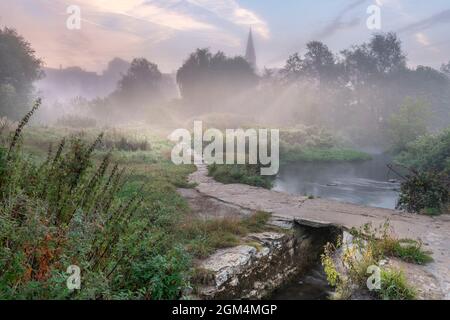 Der frühe Morgennebel klärt sich langsam über dem Flussweg und der alten Klapperbrücke, während die Sonne über der historischen Marktstadt Malmes am Hang aufgeht Stockfoto