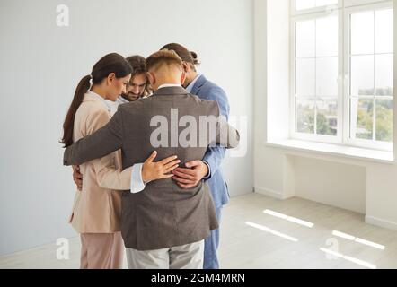 Eine Gruppe von Geschäftsleuten, die in einem engen Kreis in einem hellen leeren Raum stehen und sich umarmen. Stockfoto