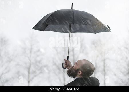 Ein kahlbärtiger Mann in einem Anzug und ein Regenschirmstock auf der Straße Stockfoto