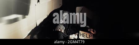 Ein obdachloser bärtiger Mann sitzt auf Kisten auf der Straße und bittet um Hilfe. Brauchen Sie eine obdachlose Person fragt nach Geld für Essen und über Nacht. Stockfoto