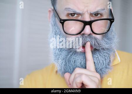 Fröhlicher Hipster-Mann mit weißem Bart. Überraschender Mann mit Brille sieht vorne. Stockfoto