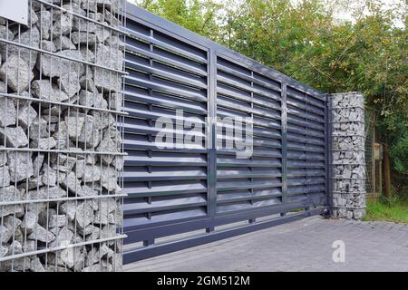 Automatisches Eingangstor in Kombination mit einer Wand aus Gabion. Stockfoto