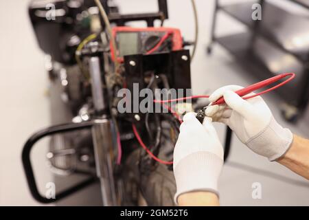 Männlicher Mechaniker, der die Elektrik des Motorrads mithilfe des Testers in Nahaufnahme überprüft Stockfoto