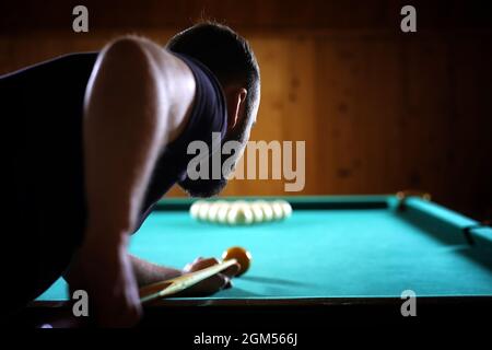 Ein Mann mit einem Bart spielt eine große Billard. Partei in 12-Fuß-Pool. Billard im Club Spiel für Männer. Ein Mann mit einer Cue bricht die Pyramide. Stockfoto