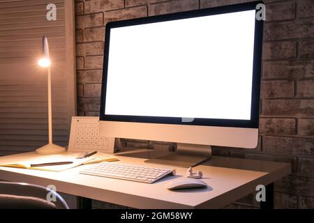 Stilvoller Arbeitsplatz mit modernem Computer und Lampe am Abend Stockfoto