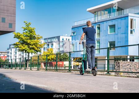 Junger Mann, der in Malmö auf einem Elektroroller durch die Straßen fährt. Stockfoto