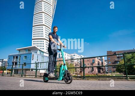 Junger Mann, der in Malmö auf einem Elektroroller durch die Straßen fährt. Stockfoto