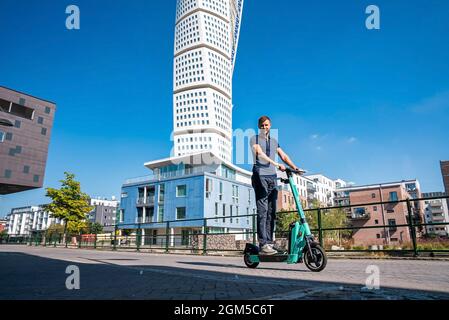 Junger Mann, der in Malmö auf einem Elektroroller durch die Straßen fährt. Stockfoto