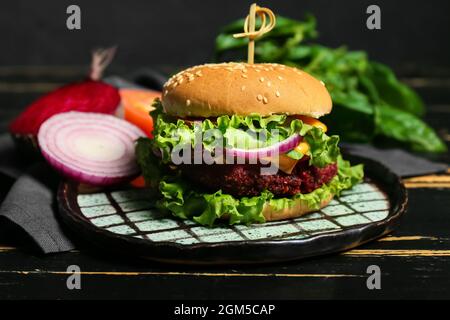 Teller mit leckeren vegetarischen Burger auf dunklem Holzhintergrund Stockfoto