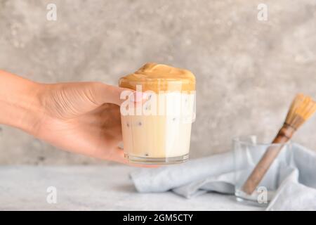 Frau hält ein Glas leckeren dalgona hojicha Latte am Tisch Stockfoto