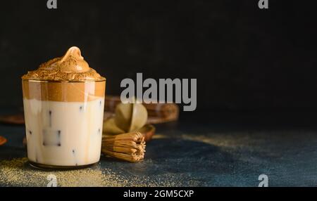 Ein Glas leckeren Dalgona hojicha Latte und Chasen auf dunklem Hintergrund Stockfoto