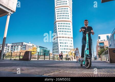 Junger Mann, der in Malmö auf einem Elektroroller durch die Straßen fährt. Stockfoto