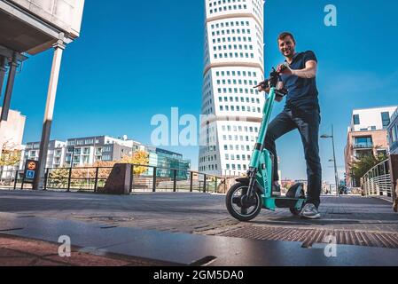 Junger Mann, der in Malmö auf einem Elektroroller durch die Straßen fährt. Stockfoto