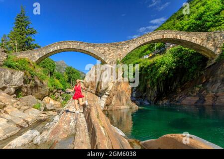 Frau, die unter der römischen Steinbrücke läuft: Ponte dei Salti über dem Verzasca-Fluss. Verzasca Tal bei Lavertezzo. Berühmtes Wahrzeichen für Freizeit am Fluss und Stockfoto